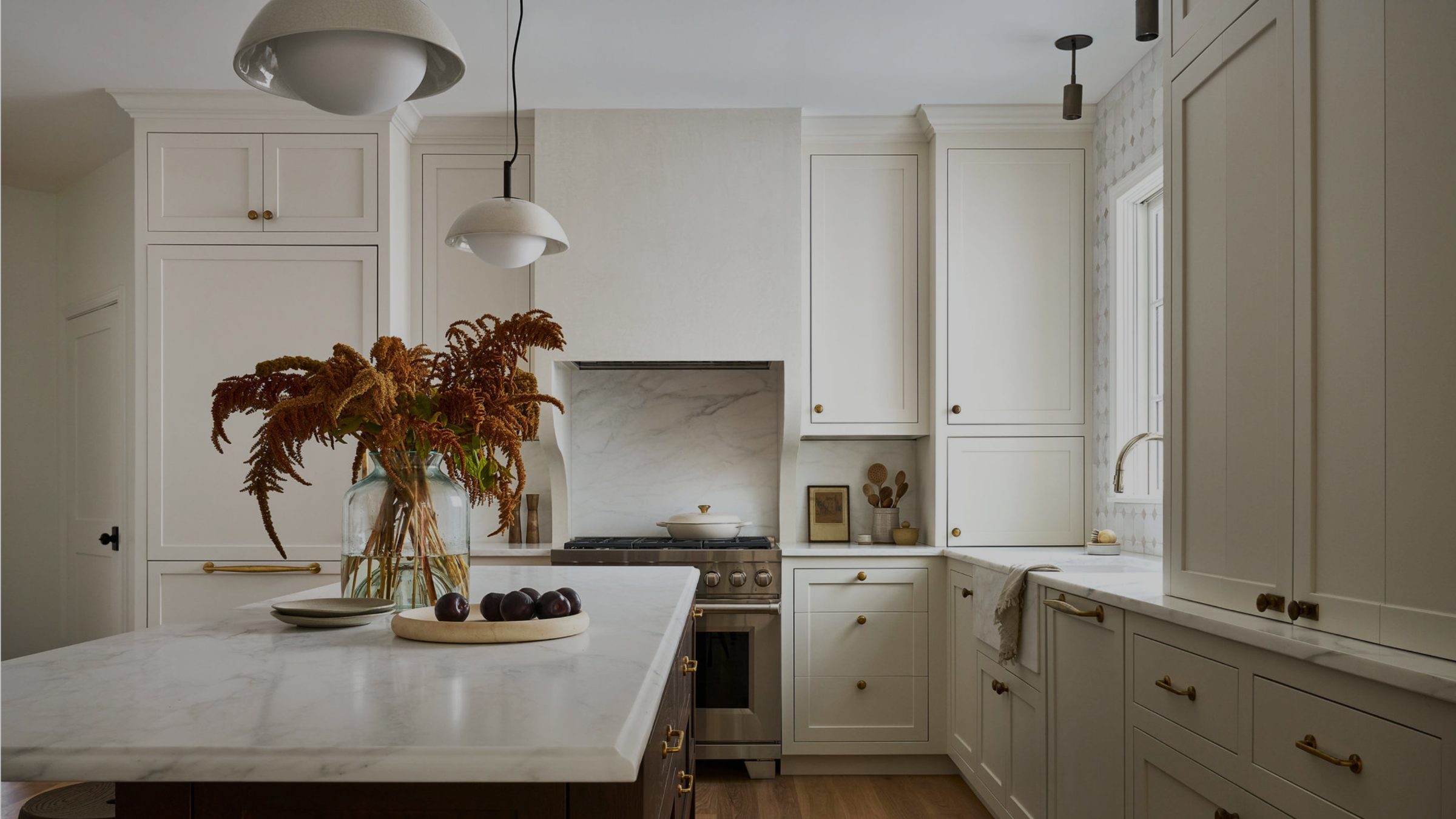 Warm white kitchen with a marble island, brass hardware, and dried florals by a TALD interior designer